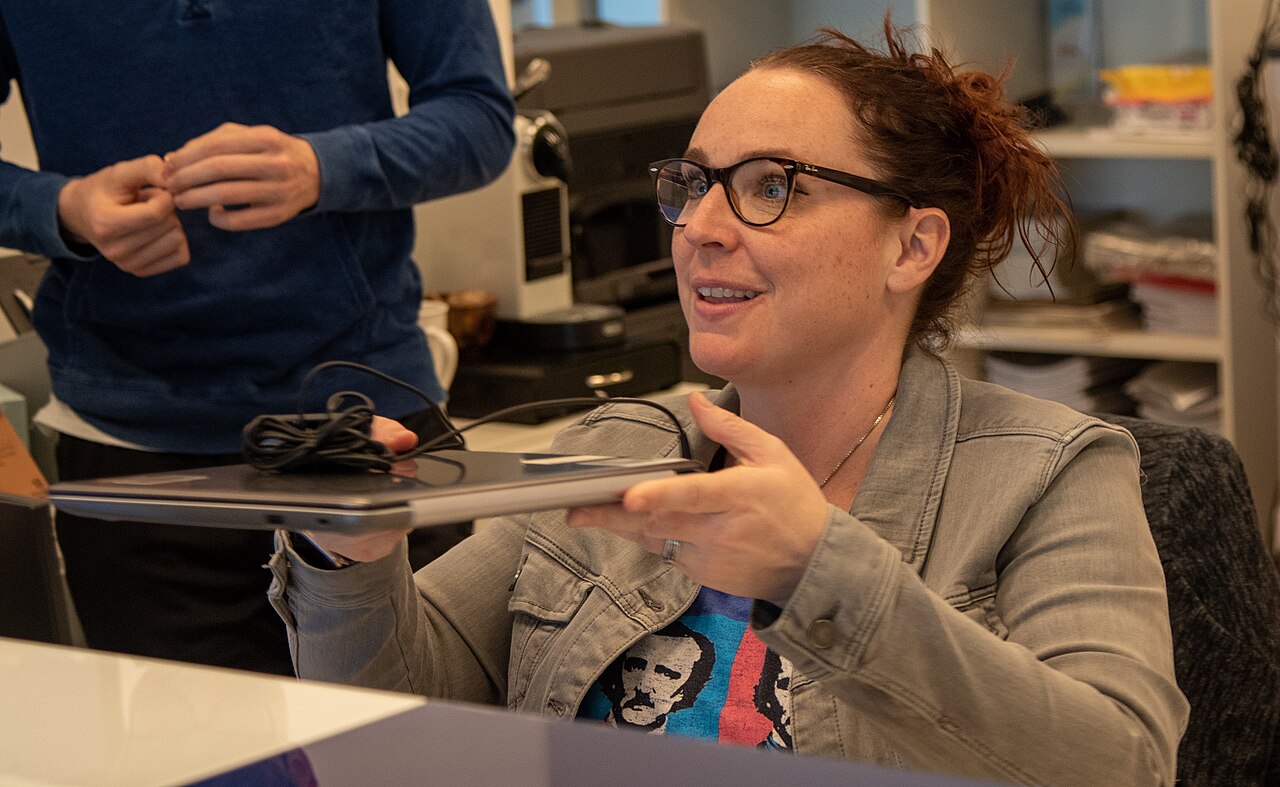 A woman handing a laptop to a student for online classes