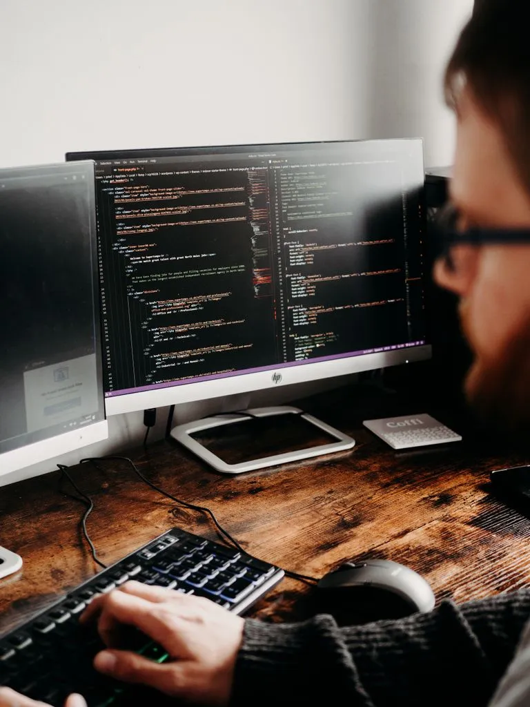 A software developer coding at a desk with multiple monitors showing code