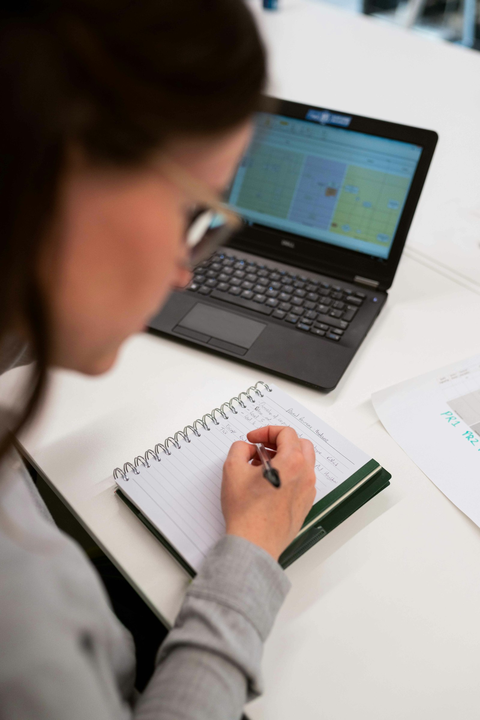 Writing study notes in a notebook beside a laptop while learning Excel
