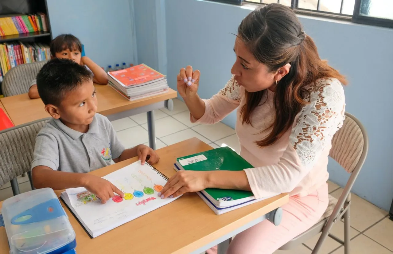 Teacher talking with a student about a workbook exercise in a bright classroom