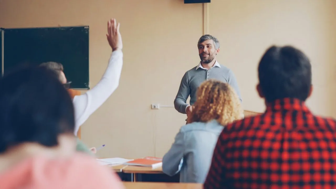 Teacher answering questions from students at the front of a classroom