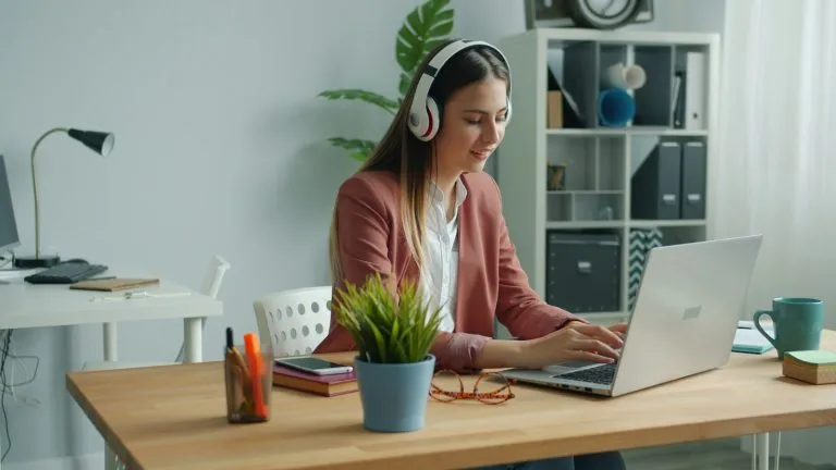 Woman wearing headphones working on a laptop at a home office desk while learning how to become a virtual assistant with no experience