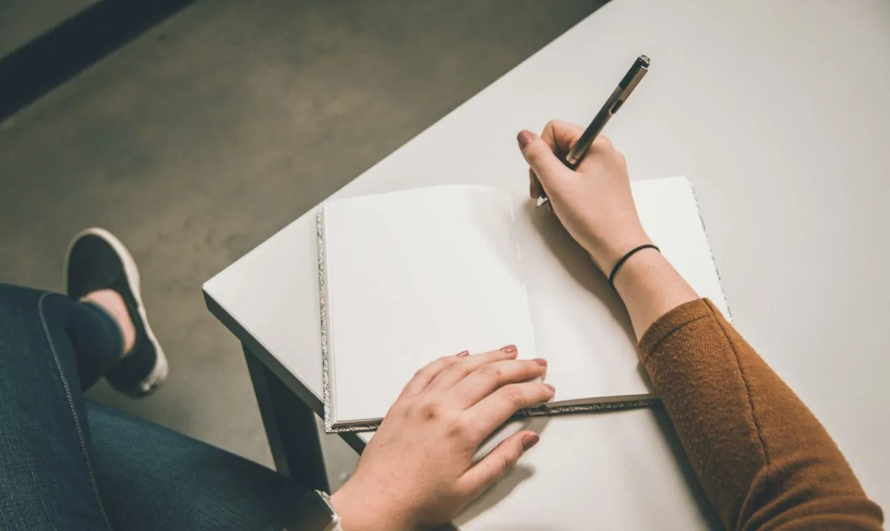 Overhead view of a student hand-writing the first draft of an essay in an open notebook