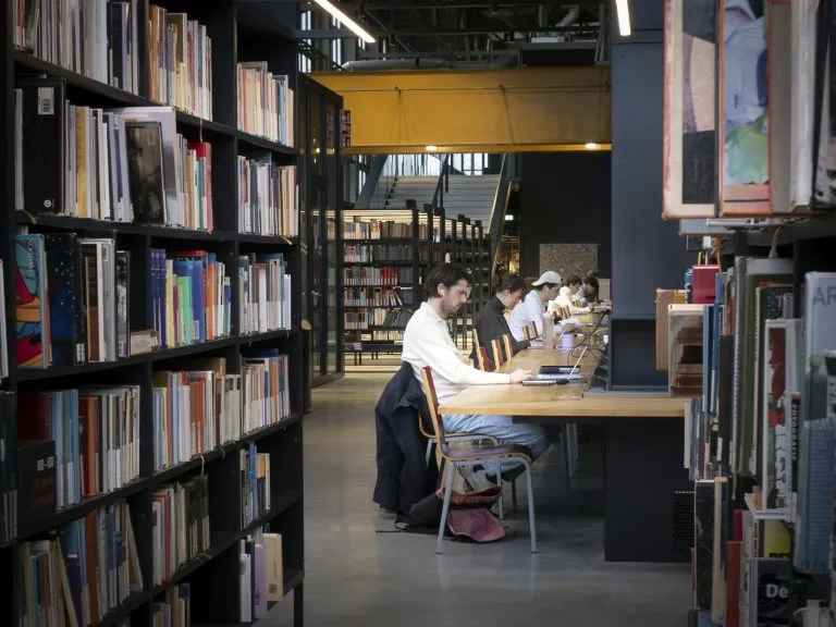 High school students studying together with books and laptops in a bright library while preparing for the national merit scholarship
