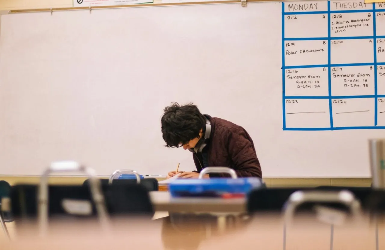 High school student writing at a classroom desk during a test