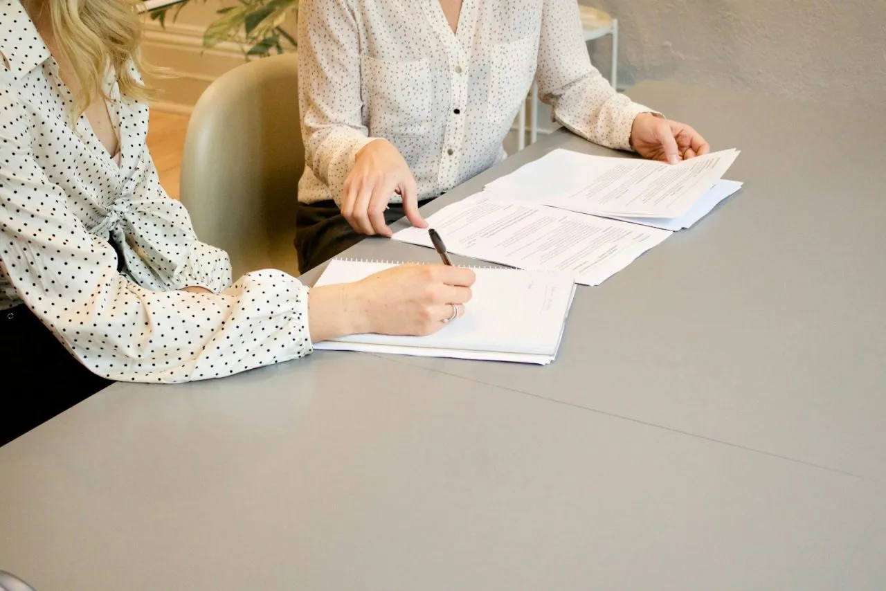 Two colleagues reviewing and signing a written job offer at a table