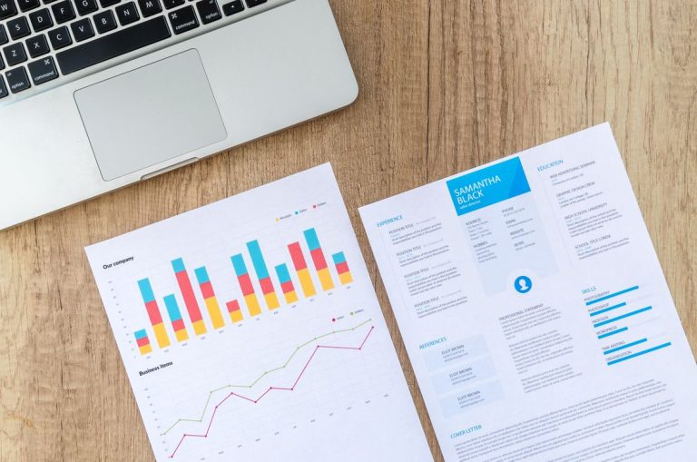 how to write a resume — resume and charts beside a laptop on a desk